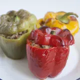Tres pimientos rellenos, uno rojo, uno verde y uno amarillo, servidos en un plato blanco con borde azul.