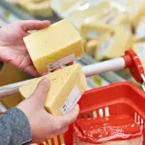 Manos sostienen trozos de queso cheddar, buscando opciones sin lactosa en el supermercado.