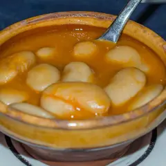 Un cuenco de barro rebosante de judiones de la granja en una salsa dorada, con una cuchara lista para servir.