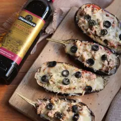 Berenjenas rellenas gratinadas con queso y aceitunas negras, junto a una botella de aceite de oliva virgen extra Oleoestepa.