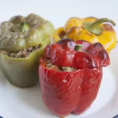 Tres pimientos rellenos, uno rojo, uno verde y uno amarillo, servidos en un plato blanco con borde azul.