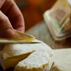 Mano cortando un queso de Tetilla con un cuchillo. Se ve la corteza blanca y el interior cremoso.