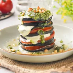 Deliciosa milhoja de berenjena con tomate, mozzarella fundida y pesto, coronada con piñones. Un plato ligero y sabroso.