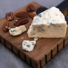 Un trozo de queso azul, ideal para la flora intestinal, reposa sobre una tabla de madera junto a nueces pecanas.