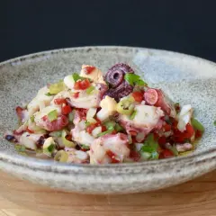 Un refrescante salpicón de pulpo con pimientos, cebolla y aceitunas, servido en un cuenco rústico.