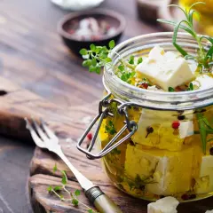 Queso en aceite de oliva, con hierbas aromáticas y granos de pimienta, listo para disfrutar.