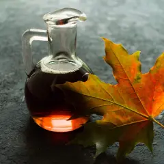 Botella de vidrio con líquido ámbar, que es el sirope de arce, junto a una hoja de arce otoñal.