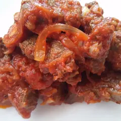 Un plato humeante de carne con tomate y cebolla, cocinado a fuego lento hasta que la carne esté tierna y la salsa espesa.
