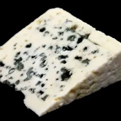 Un trozo de queso Roquefort con vetas azules y verdes, mostrando cómo se hace el queso roquefort con gusanos.