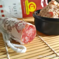 Un trozo de fuet extra con su interior rosado y veteado, junto a un cuenco de paté.