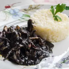Deliciosos calamares en su tinta, servidos con arroz blanco y decorados con perejil fresco.