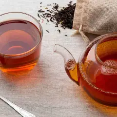 Una taza y tetera de té negro, con hojas secas esparcidas. ¿A que sabe el té negro? A un sabor robusto y reconfortante.