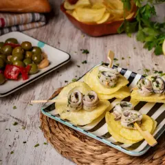 Deliciosas recetas con anchoas: pinchos de anchoas enrolladas sobre patatas fritas, acompañadas de aceitunas y limón.