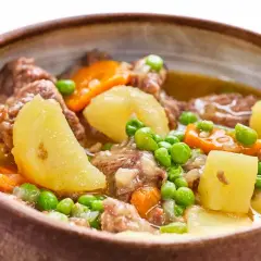 Un reconfortante ragú de ternera con patatas, zanahorias y guisantes en un cuenco de barro.