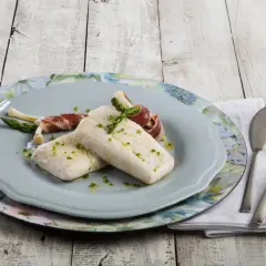 Dos lomos de merluza confitada, tiernos y jugosos, acompañados de espárragos envueltos en jamón.
