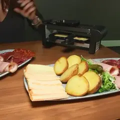 Platos con patatas, embutidos y queso listos para preparar deliciosas recetas raclette en la parrilla.
