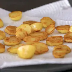 Rodajas doradas de patatas al horno, recién salidas de la sartén y escurriendo el exceso de aceite sobre papel de cocina.