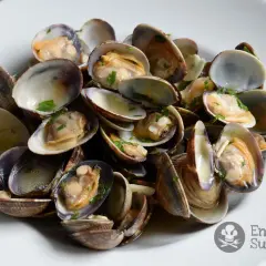Un plato de almejas a la marinera, recién cocinadas y espolvoreadas con perejil picado.