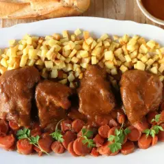 Delicioso jarrete de ternera estofado en salsa, acompañado de patatas fritas y zanahorias.