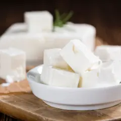 Cubos de queso blanco en un cuenco, con un bloque de queso de leche cruda al fondo. El queso de leche cruda puede presentar peligros.