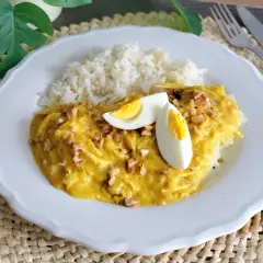 Un plato de aji de pollo cremoso con arroz blanco, huevo duro y nueces picadas.