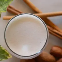 Un vaso de leche espumosa, canela y hojas verdes, recordatorio de los beneficios de la leche de vaca para una vida saludable.