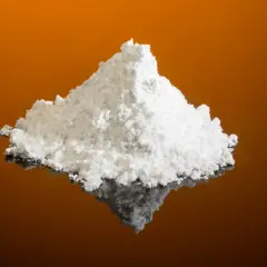 Montículo de polvo blanco fino, que es el cremor tártaro, sobre una superficie reflectante naranja.