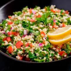 Delicioso tabule receta, una ensalada fresca de bulgur, tomate, perejil y cebolla morada, adornada con rodajas de limón.