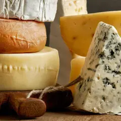 Variedad de quesos, incluyendo un trozo de queso azul y ruedas de queso, algunos de que quesos son pasteurizados.
