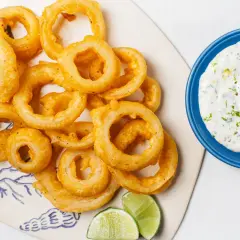 Crujientes aros de cebolla dorados, servidos con una cremosa salsa y gajos de lima. ¡Un aperitivo irresistible!