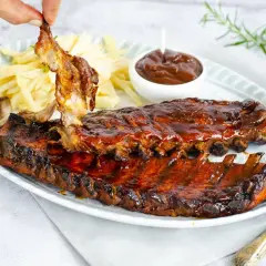 Costillas a la barbacoa jugosas y glaseadas, servidas con patatas fritas y salsa barbacoa. ¡Un festín para los sentidos!