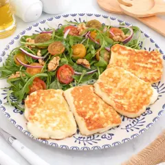 Ensalada fresca con tomates cherry, cebolla morada y nueces, acompañada de trozos dorados de ser halloumi a la plancha.