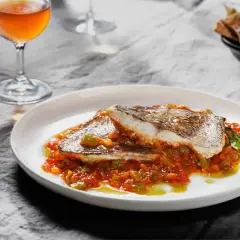 Deliciosa urta a la roteña servida en plato blanco, con guarnición de pimientos y tomate. Acompañada de copa de vino y pan.