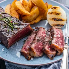 Jugoso entrecot a la plancha, cortado en rodajas, acompañado de patatas gajo y cebolla a la parrilla.