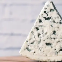 Un trozo triangular de queso azul, con sus características vetas de moho azul verdoso, descansa sobre una superficie de madera.