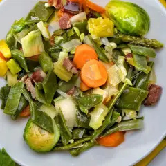 Un plato de menestra de verduras con judías verdes, zanahorias, puerros y trozos de jamón.