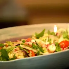 Deliciosa insalata di mare con tentáculos de pulpo, tomates cherry y hojas verdes frescas en un plato azul claro.