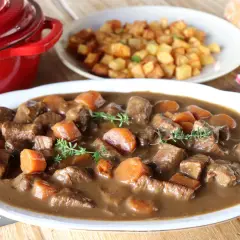 Ternera estofada en salsa con zanahorias y patatas fritas al fondo.