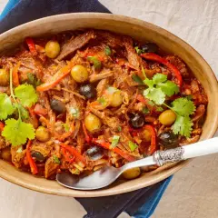Delicioso plato de ropa vieja con aceitunas verdes y negras, pimientos rojos y cilantro fresco, servido en una cazuela de barro.