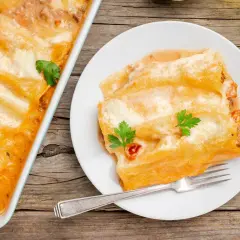 Canelones de atún gratinados, cubiertos de salsa y queso, servidos en un plato blanco con un tenedor.