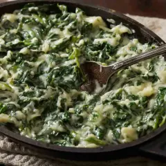 Cremosas espinacas a la crema, servidas en una sartén de hierro fundido con una cuchara lista para servir.