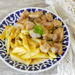 Raxo con patatas, un plato tradicional gallego, servido en un plato azul y blanco con perejil fresco.