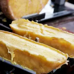 Dos mitades de queso fundido en una máquina para raclette, con el queso derritiéndose y goteando.