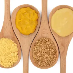 Cuatro cucharas de madera muestran la mostaza en diferentes formas: polvo, semillas y dos texturas de mostaza preparada.