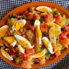 Ensalada campera con patatas, tomate, pimiento, aceitunas y huevos duros, servida en plato de barro.