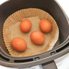 Cuatro huevos listos para convertirse en huevo duro airfryer, colocados sobre papel de hornear en la cesta de la freidora de aire.