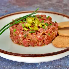 Tartar de salchichón finamente picado, adornado con pepinillos y cebollino, servido con tostas.