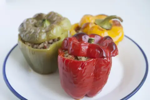 Tres pimientos rellenos, uno rojo, uno verde y uno amarillo, servidos en un plato blanco con borde azul.