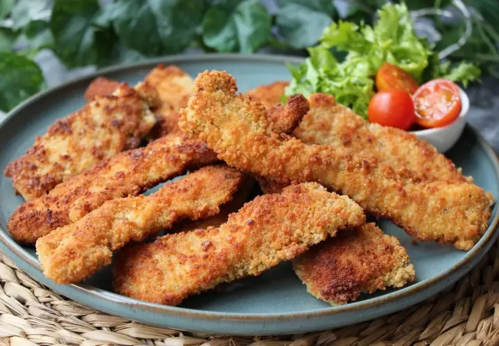 Crujientes fingers de pollo dorados, servidos en un plato azul con una guarnición de lechuga y tomates cherry. ¡Perfectos para cualquier ocasión!