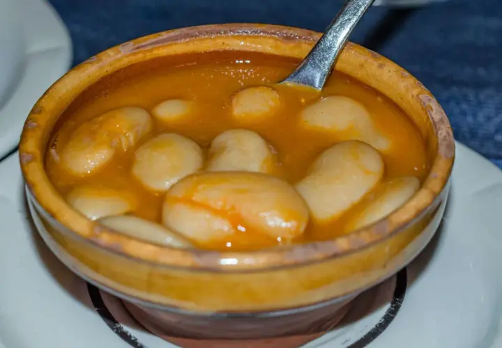 Un cuenco de barro rebosante de judiones de la granja en una salsa dorada, con una cuchara lista para servir.